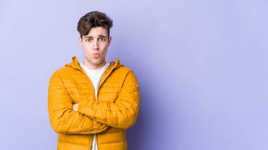 Mor arka planda izole edilmiş genç beyaz adamın yanakları şişer, yorgun bir ifadesi vardır. Yüz ifadesi kavramı.