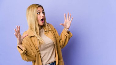 Mor arka planda izole edilmiş genç sarışın kadın gökyüzüne haykırıyor, yukarı bakıyor, hayal kırıklığına uğramış..