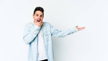 Beyaz arka planda izole edilmiş genç beyaz bir adam bir avuç içinde fotokopi alanı tutuyor, el üstünde tutuyor. Şaşırmış ve mutlu..