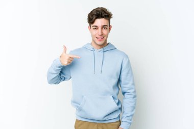 Beyaz arka planda yaşayan beyaz tenli genç bir adam gömlek fotokopi alanını gösteriyor, gururlu ve kendinden emin.