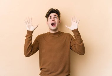 Kafkasyalı genç adam bej arka planda izole edilmiş gökyüzüne haykırıyor, yukarı bakıyor, hayal kırıklığına uğramış.