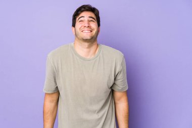 Mor arka planda soyutlanmış genç adam gülüyor ve gözlerini kapatıyor, rahatlamış ve mutlu hissediyor..