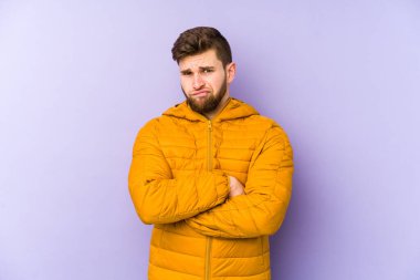 Genç adam mor arka planda izole edilmiş, mutsuz ve alaycı bir ifadeyle kameraya bakıyor..