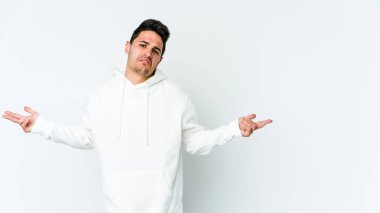 Beyaz arka planda izole edilmiş genç beyaz bir adam sorgulama sırasında omuz silkiyor ve şüphe duyuyor..