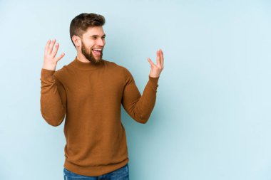 Kafkasyalı genç adam mavi arka planda izole edilmiş neşeli bir şekilde gülüyor. Mutluluk kavramı.