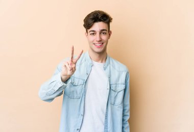 Beyazların arka planında izole edilmiş genç beyaz adam zafer işareti gösteriyor ve gülümsüyor..