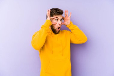 Mor arka planda izole edilmiş genç beyaz adam bir başarı fırsatı bulmak için gözlerini açık tutuyor..