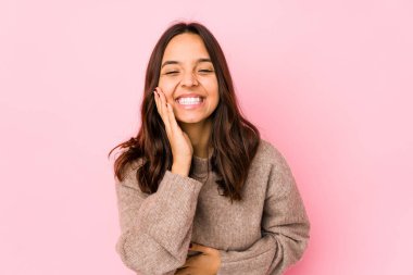 Genç melez İspanyol kadın mutlu bir şekilde gülüyor ve ellerini karnının üstünde tutarak eğleniyor..