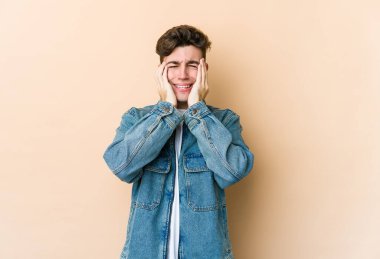 Beyaz tenli genç adam bej arka planda izole edilmiş ağlıyordu, bir şeyden mutsuzdu, ıstırap ve kafa karışıklığı vardı..