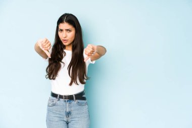 Mavi arka planda genç Hintli kadın baş parmağını aşağı gösteriyor ve hoşlanmadığını ifade ediyor..