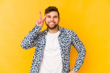 Sarı arka planda izole edilmiş genç beyaz adam iki numarayı parmaklarıyla gösteriyor..