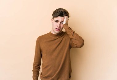 Beyazlı genç bir adam bej arka planda izole edilmiş. Yorgun ve uykulu. Elini başının üstünde tutuyor..