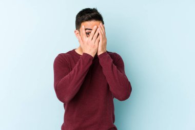 Kafkasyalı genç adam mavi arka planda izole edilmiş. Korkmuş ve gergin parmaklarıyla göz kırp..