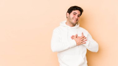 Bej arka planda izole edilmiş genç bir adam, dostane bir ifadeye sahip, avuçlarını göğsüne bastırıyor. Aşk konsepti.