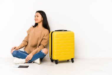 Genç Çinli gezgin bir bavulla yerde oturuyor. Tek başına. Gülümsüyor, neşeli ve keyifli..