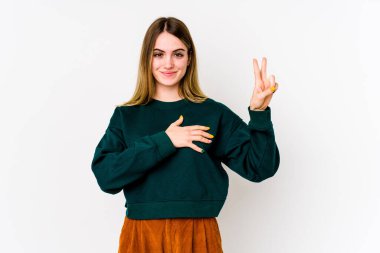 Beyaz arka planda izole edilmiş genç beyaz kadın yemin ediyor, elini göğsüne koyuyor..