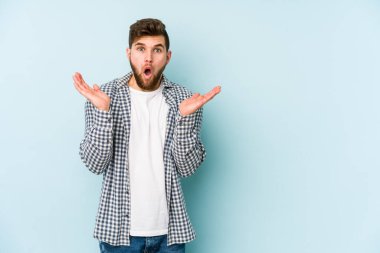 Kafkasyalı genç adam mavi arka planda izole edildi. Şaşırdı ve şok oldu..