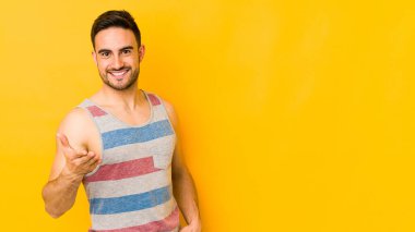 Sarı fırında izole edilmiş genç beyaz adam kameraya elini uzatarak selam veriyor..