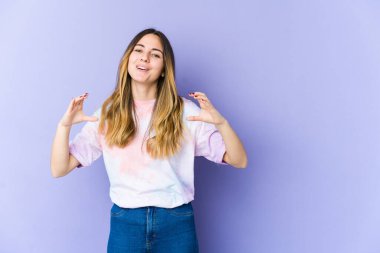 Mor arka planda izole edilmiş beyaz bir kadın avuçlarıyla bir şey tutuyor ve kameraya sunuyor..