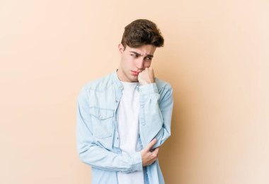 Bej arka planda izole edilmiş, üzgün ve dalgın hisseden, fotokopi alanına bakan genç beyaz bir adam..