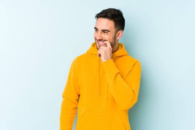 Mavi arka planda izole edilmiş genç beyaz adam rahatlamış bir şeyin fotokopi odasına baktığını düşünüyor..