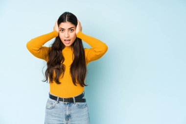 Genç Hintli kadın mavi arka planda izole edilmiş bağırıyor, çok heyecanlı, tutkulu, bir şeyden memnun..