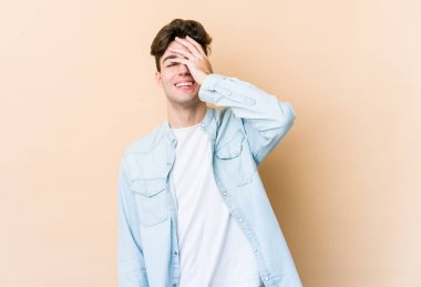 Beyaz tenli genç adam bej arka planda izole edilmiş gülerek, kaygısız, doğal duygularla gülüyor..