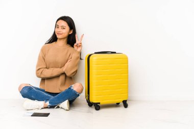 Genç Çinli gezgin kadın iki numarayı parmaklarıyla göstererek izole edilmiş bir bavulla yerde oturuyor..