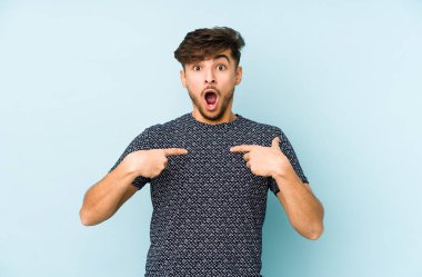 Mavi arka planda izole edilmiş genç bir Arap parmak göstererek şaşırdı, geniş bir gülümsemeyle..