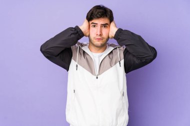 Mor arka planda izole edilmiş genç bir adam kulakları elleriyle kapatıyor ve yüksek sesli sesler duymamaya çalışıyor..