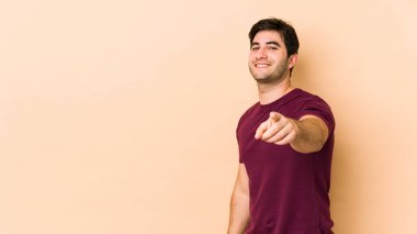 Bej arka planda izole edilmiş genç adam parmaklarıyla ön tarafı işaret ediyor..