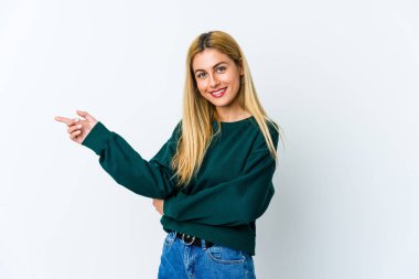 Beyaz arka planda izole edilmiş genç sarışın kadın işaret parmağıyla işaret ederek gülümsüyor..