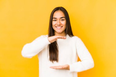 Sarı arka planda izole edilmiş genç bir kadın iki eliyle bir şey tutuyor, ürün sunumu..