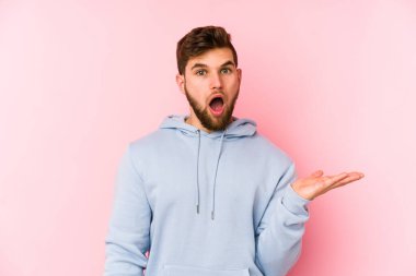 Pembe arka planda izole edilmiş genç beyaz adam, avuç içi fotokopi alanını elinde tutmaktan etkilenmiş..
