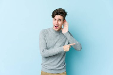 Mavi arka planda izole edilmiş genç beyaz adam bir dedikoduyu dinlemeye çalışıyor..