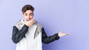 Mor arka planda izole edilmiş genç beyaz bir adam avuç içinde fotokopi alanı tutuyor, el üstünde tutuyor. Şaşırmış ve mutlu..