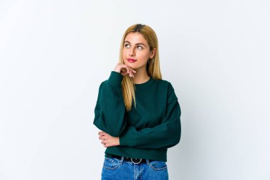 Beyaz arka planda izole edilmiş genç sarışın kadın şüpheli ve şüpheci bir ifadeyle yana bakıyor..