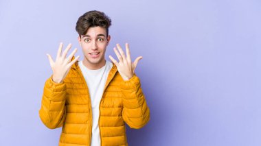 Mor arka planda izole edilmiş genç beyaz adam on numarayı elleriyle gösteriyor..