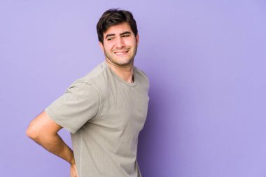 Mor arka planda izole edilmiş genç bir adam sırt ağrısı çekiyor..