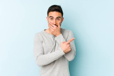 Mavi arka planda izole edilmiş genç beyaz adam yan tarafı işaret ediyor.