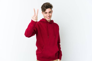 Beyaz arka planda izole edilmiş genç beyaz bir adam zafer işareti gösteriyor ve gülümsüyor..