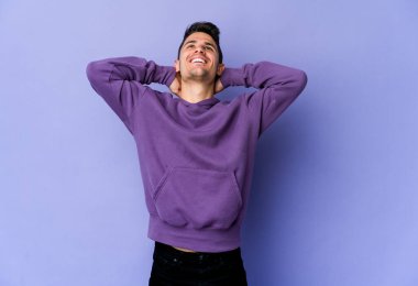 Mor arka planda izole olmuş genç beyaz bir adam kendini güvende hissediyor, elleri başının arkasında..