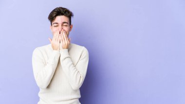 Mor arka planda izole olmuş genç beyaz bir adam bir şeye gülüyor, elleriyle ağzını kapatıyor..