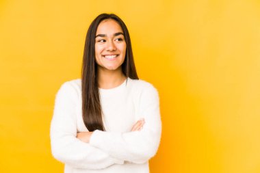 Sarı arka planda izole edilmiş genç bir kadın kollarını kavuşturarak gülümsüyor..