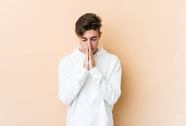 Beyaz tenli genç adam bej arka planda izole edilmiş dua ediyor, bağlılık gösteriyor, dindar biri ilahi ilham arıyor..