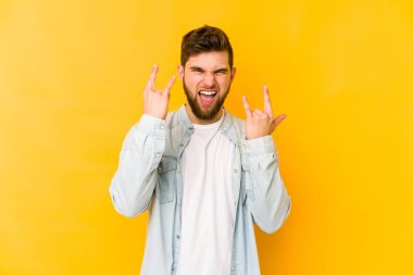 Sarı arka planda izole edilmiş genç beyaz adam boynuzlarını devrim konsepti olarak gösteriyor..