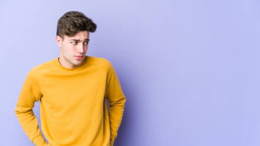 Mor arka planda soyutlanmış, kafası karışmış, şüpheli ve kararsız genç bir beyaz adam..