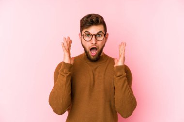 Pembe arka planda izole edilmiş genç beyaz bir adam zaferi ya da başarıyı kutluyor, şaşırıyor ve şok oluyor..