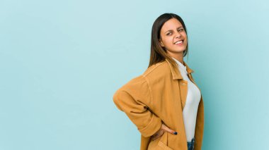 Mavi arka planda izole edilmiş, sırt ağrısı çeken genç bir kadın..