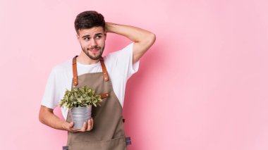 Kafkasyalı genç bahçıvan elinde bir bitki tutuyor. Kafasının arkasına dokunuyor, düşünüyor ve bir seçim yapıyor..